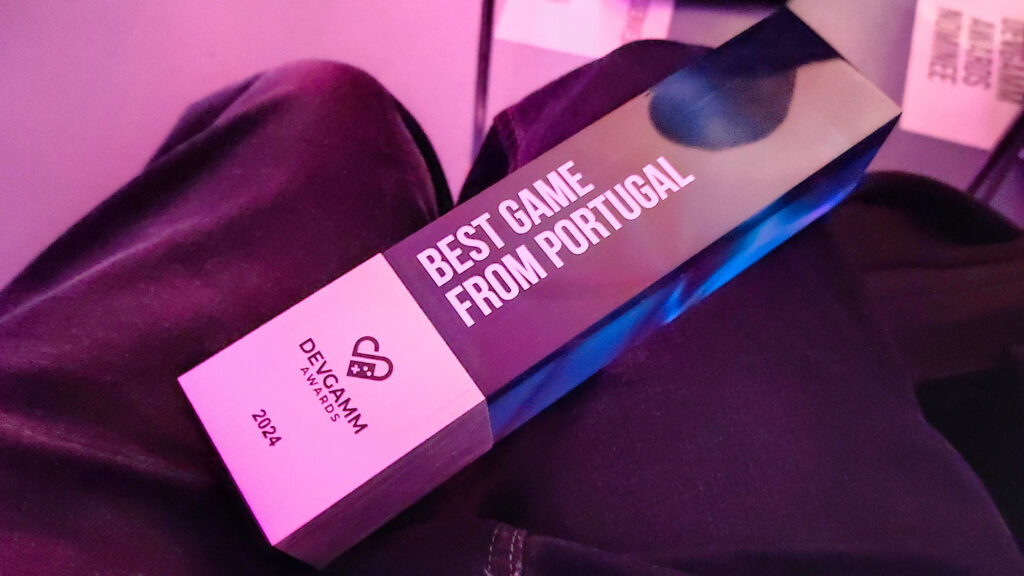 A photograph from the Best Game from Portugal trophy award, standing on top of Jorge's trousers, taken immediately after Townseek received the award. The trophy is a glass parallelogram with white letters with the name of the award and an etched metal base with the award's logo on it. Additionally, the glass also has a blue texture on the back.