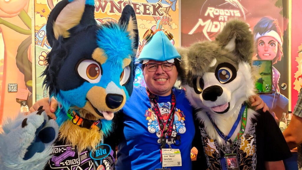 A photo of Moski taken in front of the Townseek booth during gamescom. In the picture, Moski is wearing a Townseek-themed hat and wearing his blue shirt with the Whales And Games emblem. He has two furries in fursuits to his side. with two furries in fursuits in front of the Townseek booth. The left furry is called Blu and is a dog with blue and black fur. The right furry has gray and white fur as well as heterochromia yellow and blue eyes.