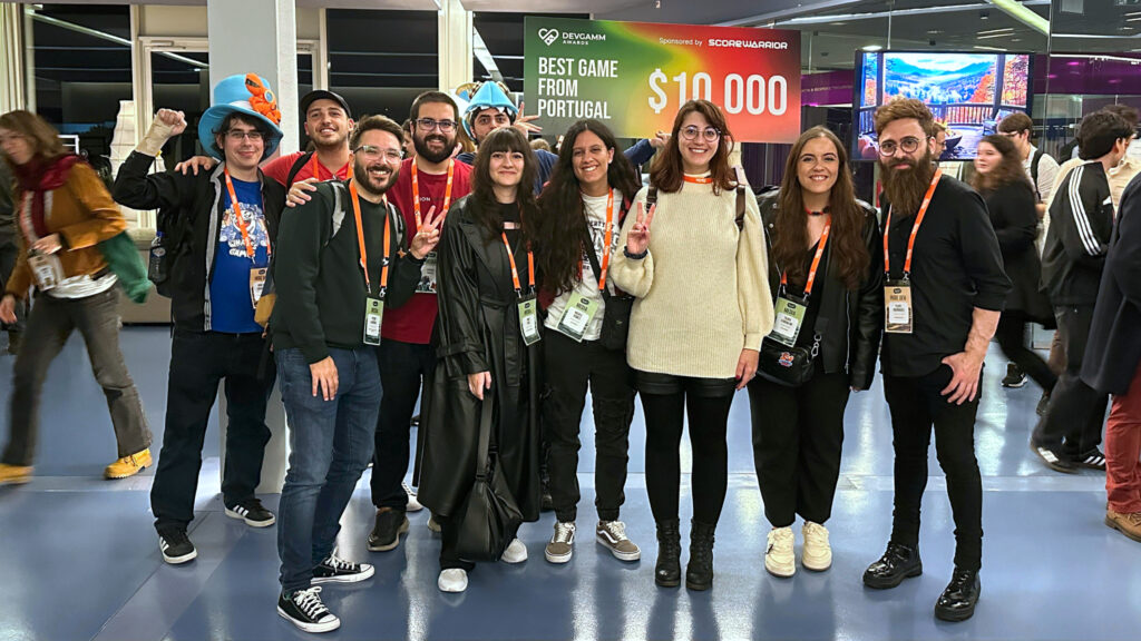 A photo from DevGAMM taken immediately after the DevGAMM Awards, showing a big group of people celebrating the achievement and their time at the event. The group is composed of both the team, other developers, and Portuguese content creators and media. Jorge is on the left of the picture doing a victory fist, while John holds the award check for Best Game from Portugal in the back.